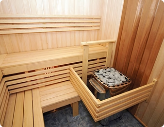 A pale wood sauna interior with a stone-filled heater set into the lower bench